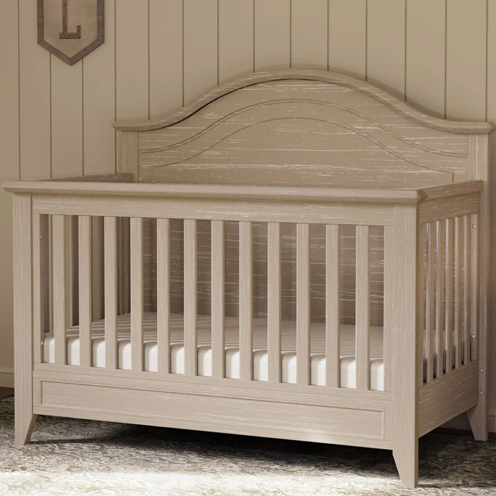 Rustic curve-top convertible crib with adjustable mattress heights in nursery setting